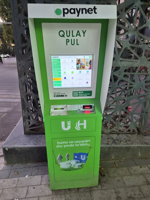 Уличный терминал Paynet «Qulay pul» у ограды с узорной решёткой: пополнение карт Humo и Uzcard