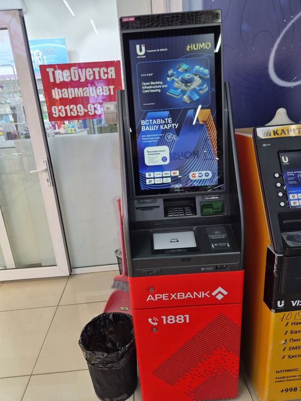 Банкомат Апексбанка с вертикальным сенсорным экраном (Uzcard, Humo) у стеклянной двери аптеки в Экобазаре; справа — банкомат Капиталбанка