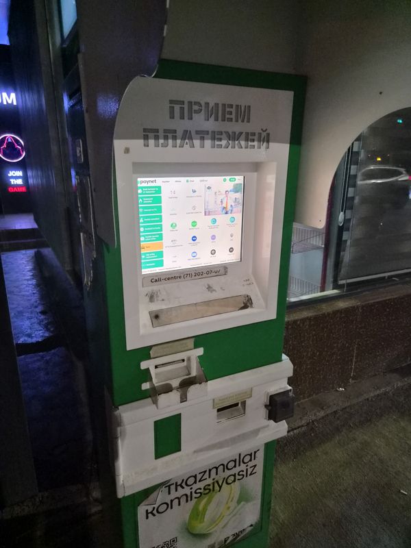 Платёжный терминал Paynet «Приём платежей» под навесом у входа: экран с услугами, приём наличных и выдача чека; наличные не выдаёт