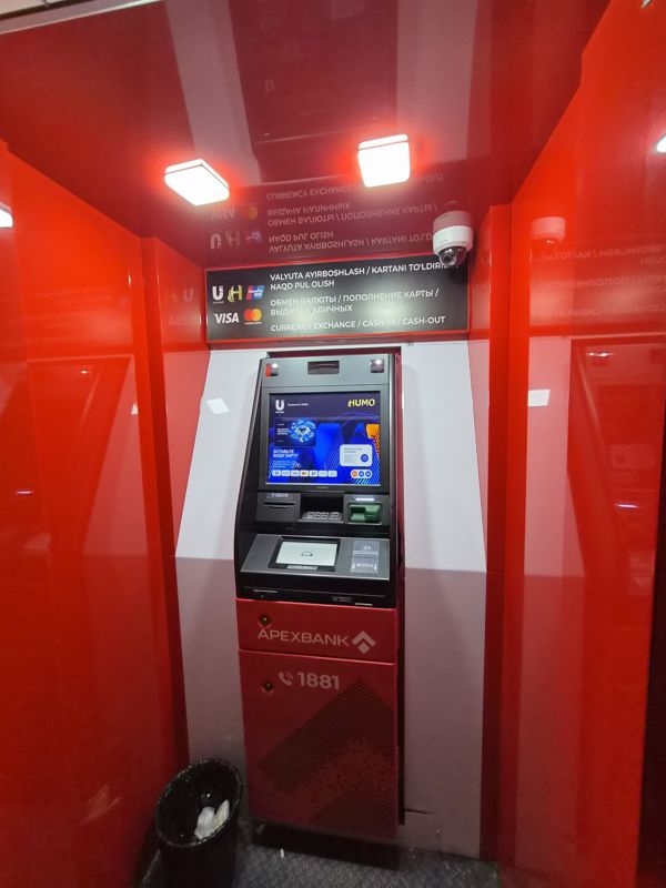 Банкомат Apexbank в красной будке: табличка «обмен валют, пополнение карты, выдача наличных», бесконтактный считыватель, call center 1881, две видеокамеры, мусорная корзина