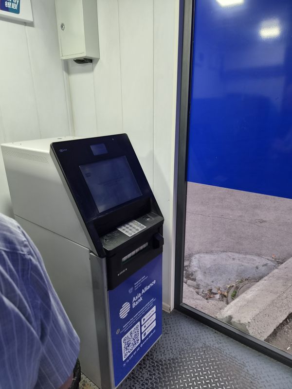 Банкомат Asia Alliance Bank (NCR) в уличной будке со стеклянной дверью: сенсорный экран, клавиатура, бесконтактный считыватель, лоток выдачи наличных; на нижней панели логотип Asia Alliance Bank, «Naqd pul olish / Выдача наличных / Cash out», QR приложения Alliance Pay, www.aab.uz и телефон 71 231 60 00; вверху слева виден знак UnionPay