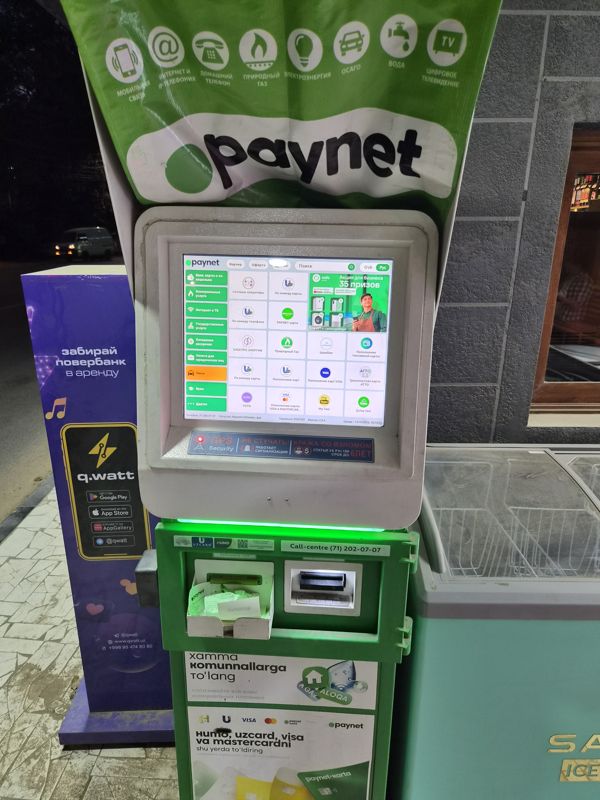 Терминал Paynet (пополнение и оплата услуг, наличные не выдаёт) на улице у магазина, рядом стойка проката повербанков q.watt