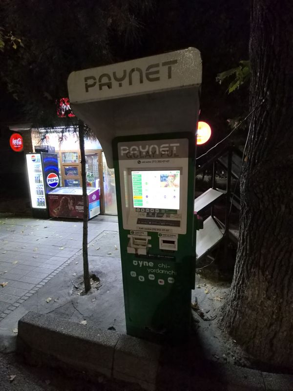 Уличный терминал Paynet «Qulay pul» на тротуаре у киоска: сенсорный экран, приёмник купюр («naqd pul kiriting»), выдача чека, карты Humo, Uzcard, Visa, call-центр (71) 202-07-07