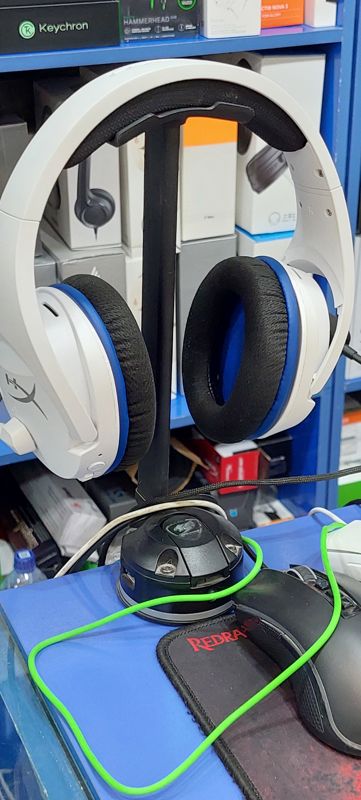 Беспроводная игровая гарнитура HyperX на стойке, рядом игровые мыши и коврик Redragon, на полках коробки Razer и Keychron