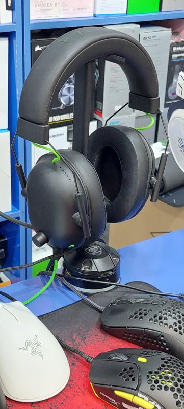 Чёрная игровая гарнитура Razer с зелёными кабелями на подставке, рядом мыши Razer и HyperX