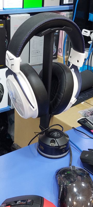 Бело-синяя игровая гарнитура на подставке Cougar, рядом игровые мыши, на полках коробки гарнитур