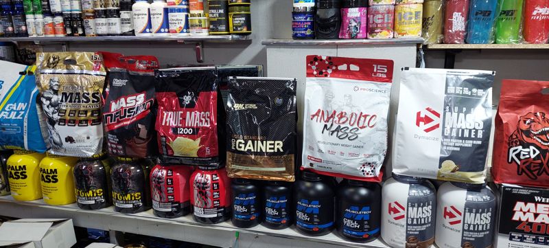 Полка с гейнерами: пакеты и банки Mass Infusion, True Mass, Pro Gainer, Anabolic Mass, Super Mass Gainer; выше витамины