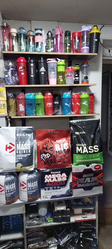 Стеллаж: спортивные бутылки и шейкеры Powergym, Reebok, Adidas, Axelus, Puma, UFC; ниже пакеты гейнеров, внизу щитки Shingard