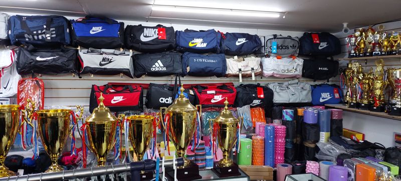 Стена со спортивными сумками Nike, Adidas, Under Armour, внизу кубки и коврики для йоги, пенные ролики