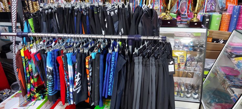Стойка со спортивными шортами и лосинами Venum, плавательные плавки; справа кубки, пенные ролики, плавательные очки