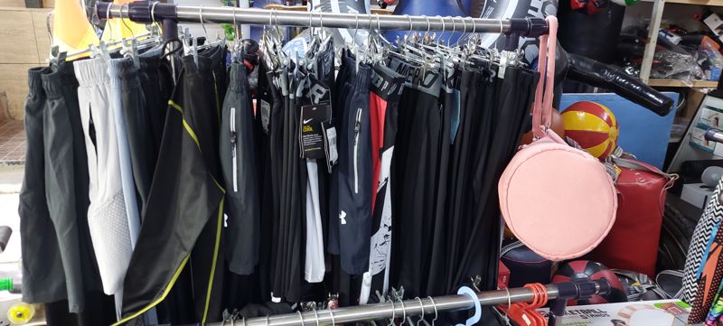 Стойка со спортивными шортами, лосинами и штанами Nike, Under Armour; справа розовая сумка, мячи-медболы, груши