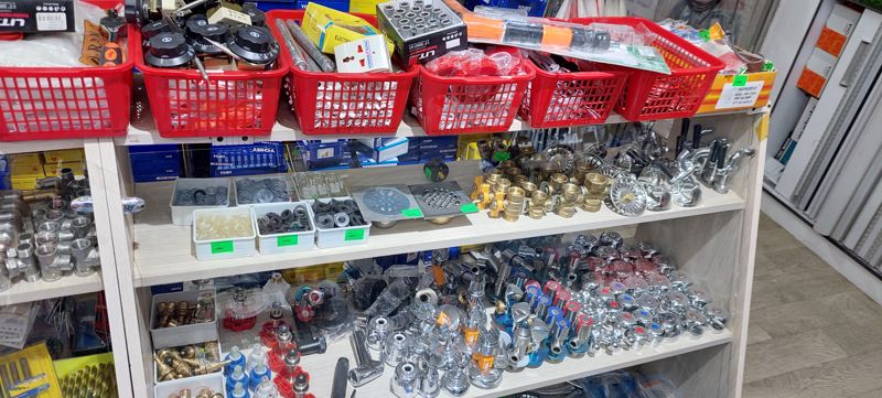 Витрина сантехнической фурнитуры: прокладки и шайбы в контейнерах по 1000 сум, трапы напольные, краны шаровые, сливные решётки раковин, угловые вентили, смесительные буксы; сверху корзины с терморегуляторами, переходниками, торцевыми головками
