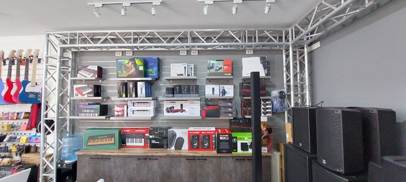 Стена магазина музыкальных инструментов: микрофоны, MIDI-клавиатуры, аудиоинтерфейсы, студийные мониторы, гитары слева
