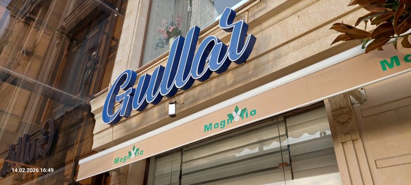 Синяя объёмная вывеска «Gullar» («цветы» по-узбекски) над входом магазина Magnolia с навесом; слева отражение вывески в стекле соседнего магазина