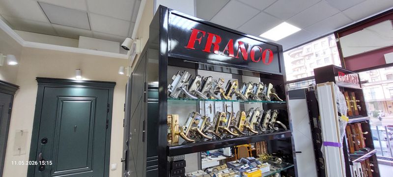 Стенд Franco с дверными ручками на врезных замках на стеклянных полках, внизу цилиндры; слева входные двери
