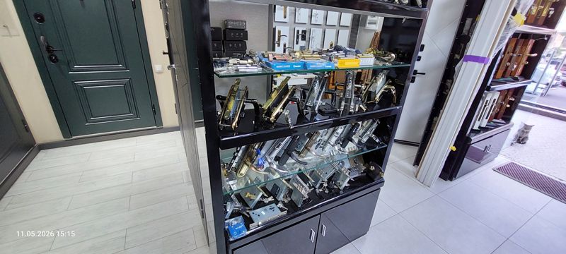 Стенд с врезными замками, ручками и цилиндрами Security Cylinder в коробках на стеклянных полках; рядом входная дверь