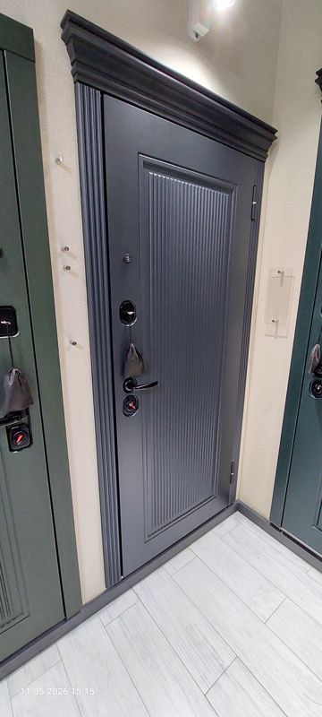 Образец входной двери тёмно-серого цвета с ребристой панелью и карнизом; рядом зелёные двери