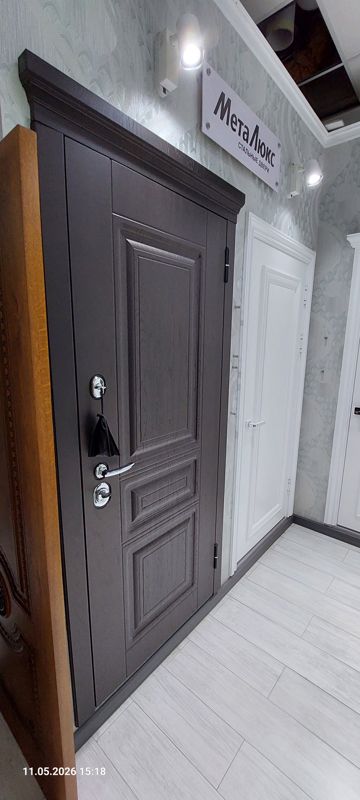Выставочный образец стальной входной двери цвета тёмного дерева с филёнками, хромированной ручкой и замками под вывеской «МетаЛюкс — стальные двери»