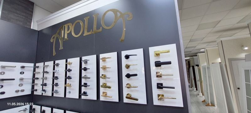 Стенд Apollo с образцами дверных ручек на белых панелях, золотая объёмная надпись «APOLLO», вдали ряд межкомнатных дверей