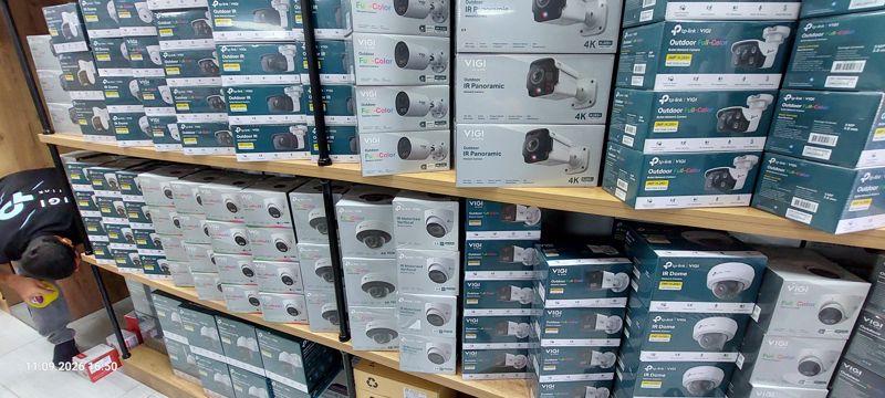 Стеллажи с камерами TP-Link VIGI: Outdoor Full-Color C330, Outdoor IR, IR Panoramic 4K, IR Motorized Varifocal 4K, IR Dome, Full-Color Dual-Lens Pan Tilt; слева внизу сотрудник на коленях у полки