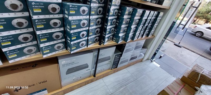 Полки с камерами TP-Link VIGI IR Mini Dome (3 Мп) и IR Dome, внизу коробки VIGI 16 Channel PoE+ NVR; справа стеклянная дверь на улицу