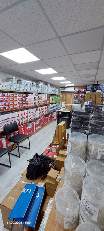 Вид вдоль торгового зала: слева стеллажи с красными коробками Hikvision, справа банки RJ45 и чёрные устройства в плёнке, на полу синие сумки tp-link