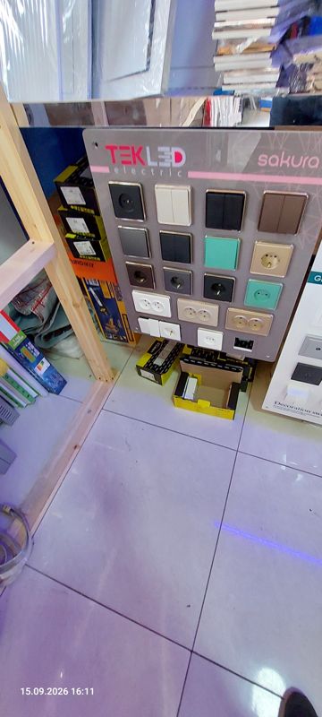 Демонстрационный стенд розеток и выключателей TEK LED electric серии Sakura: одно- и двухклавишные выключатели, розетки одинарные и двойные разных цветов; рядом коробки с электротоварами