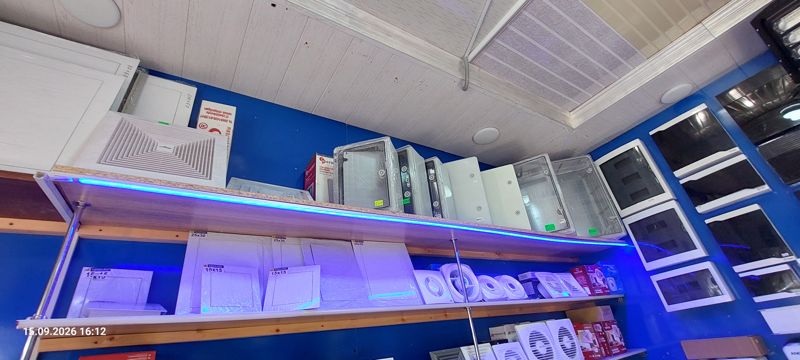 Стена с вентиляционными решётками, пластиковыми герметичными боксами, накладными электрощитками и вытяжными вентиляторами; мелкие ценники на боксах не читаются