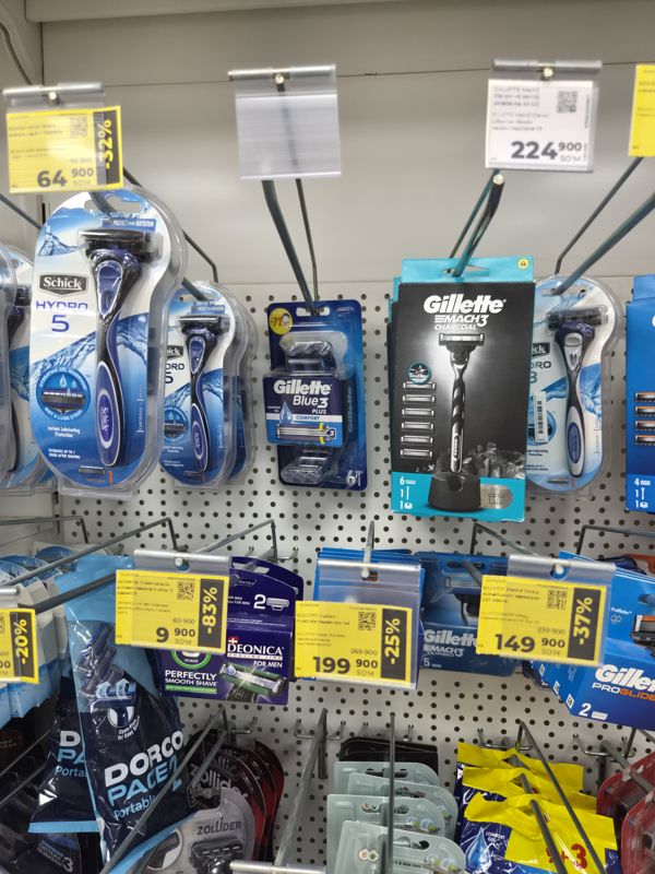 Стенд на крючках с бритвенными станками Schick, Gillette, Dorco и кассетами, жёлтые ценники со скидкой до 83%, снимок смазан