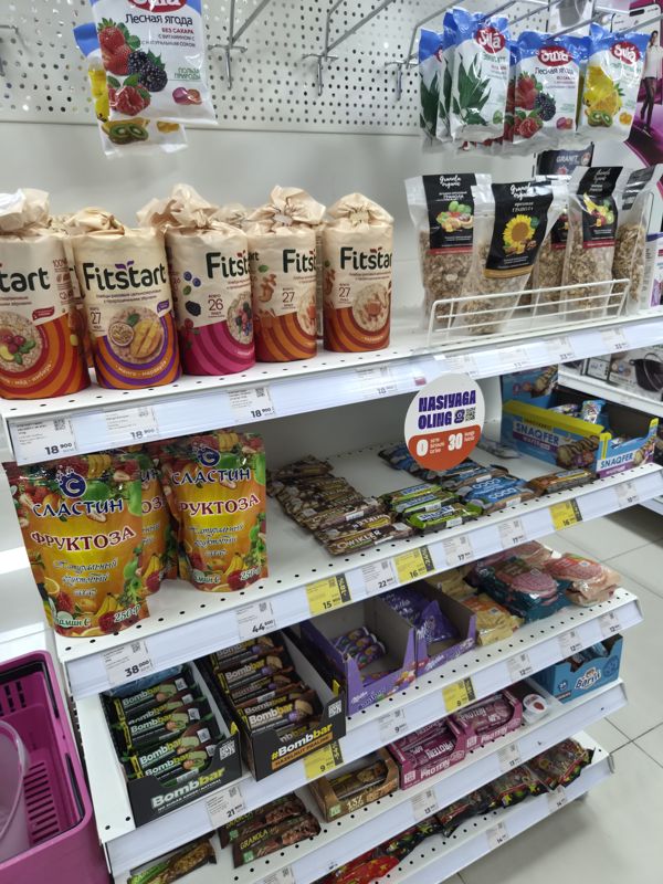Стеллаж с хлебцами Fitstart, гранолой, батончиками и драже, ценники белые и жёлтые со скидкой