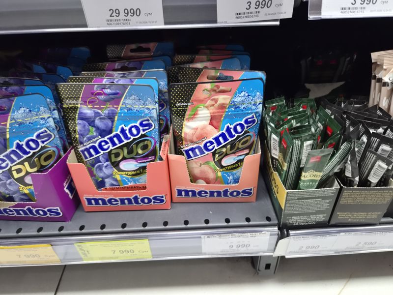 Полка с драже Mentos Duo и стиками кофе Jardin, Carte Noire и Jacobs, белые и жёлтые акционные ценники (кадр смазан)