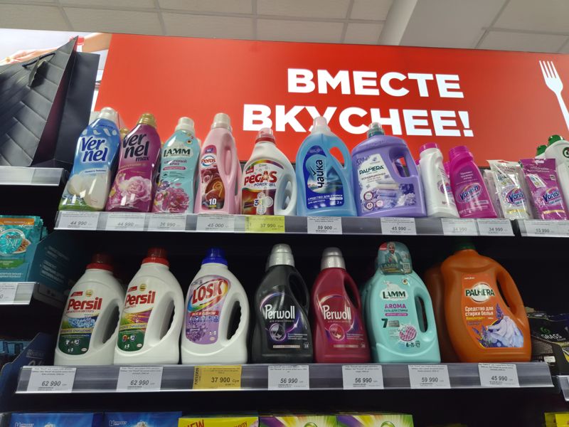 Полки со средствами для стирки и кондиционерами для белья под вывеской «Вместе вкуснее!»: верхняя полка — кондиционеры, пятновыводители, гель Pegas, нижняя — гели в бутылках