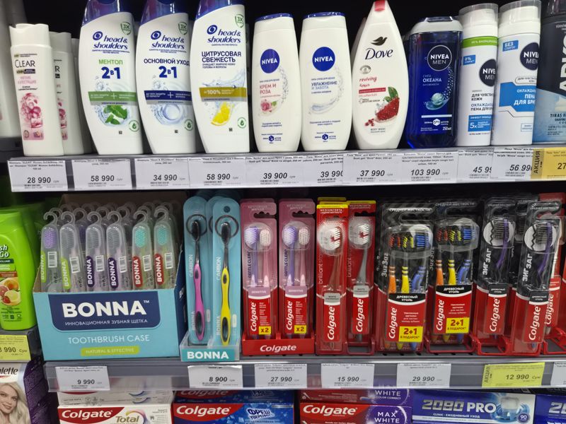Полка с шампунями, гелями для душа Nivea и Dove и зубными щётками Colgate и Bonna, белые и жёлтый акционный ценники