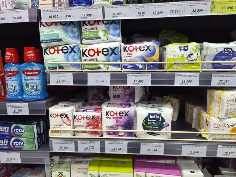 Витрина Олмы: прокладки Kotex, Bella, FREE STYLE, Peri; сверху кремы и мицеллярная вода, слева ополаскиватель Colgate и зубная паста 2080, белые ценники
