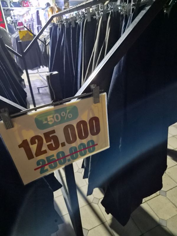 Стойка мужских брюк с табличкой «-50% 125.000», зачеркнуто 250.000
