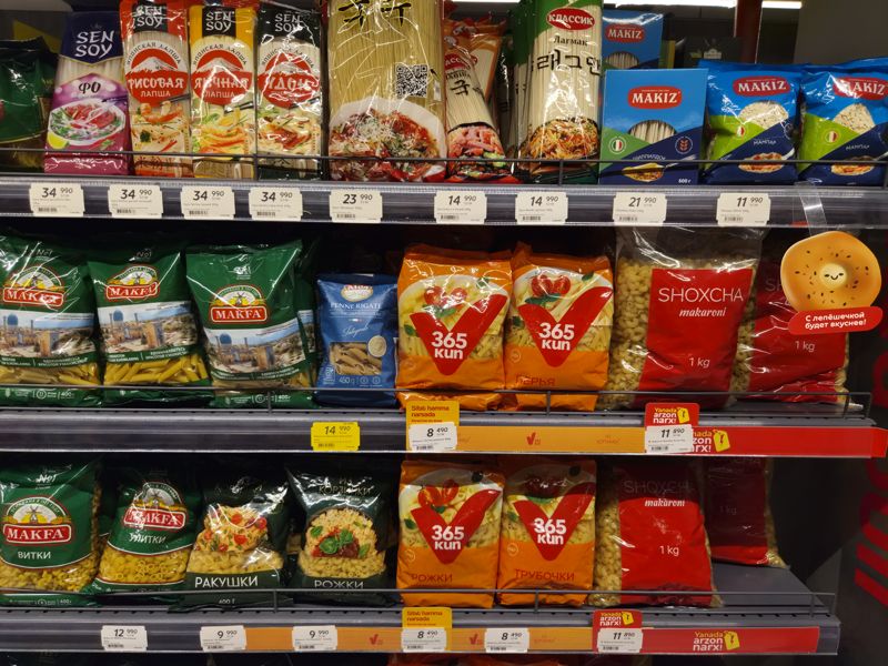 Полки с макаронами и лапшой: SenSoy, Makiz, Makfa, 365 kun, Из Корзинки, Shoxcha; белые ценники и жёлтые плашки
