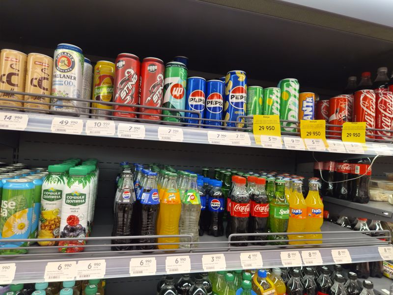 Газировка в банках на холодильной полке и бутылки 250 мл, белые ценники и жёлтые карточки Aksiya