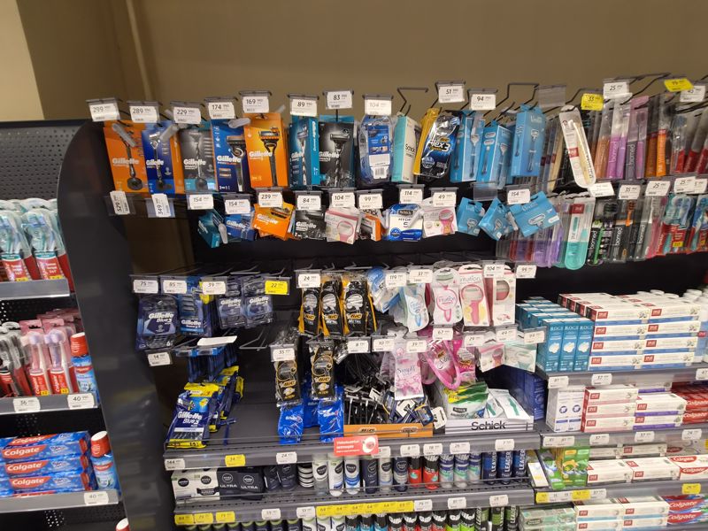 Стенд бритвенных станков и кассет Gillette, Schick, BIC, Venus, зубные щётки и пасты по бокам; общий вид отдела