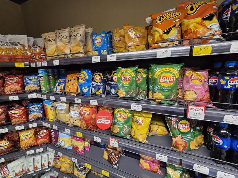 Стеллаж чипсов Lay's, Cheetos, Bon Giorno, Московский картофель, Pringles, Crash; белые, жёлтые ценники и красные плашки Narxiga javob