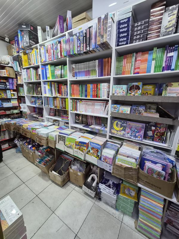 Азбука: учебники и детские книги на стеллажах, настольные игры и детские игрушки, коробки с рабочими тетрадями и ручками на полу