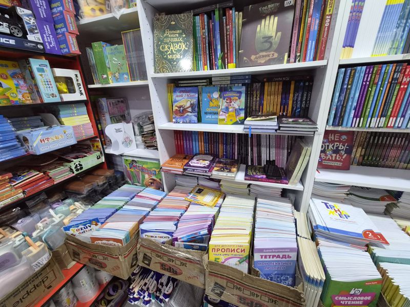Азбука: угол с книгами на белом стеллаже и красными полками с игрушками, внизу в коробках прописи и школьные тетради