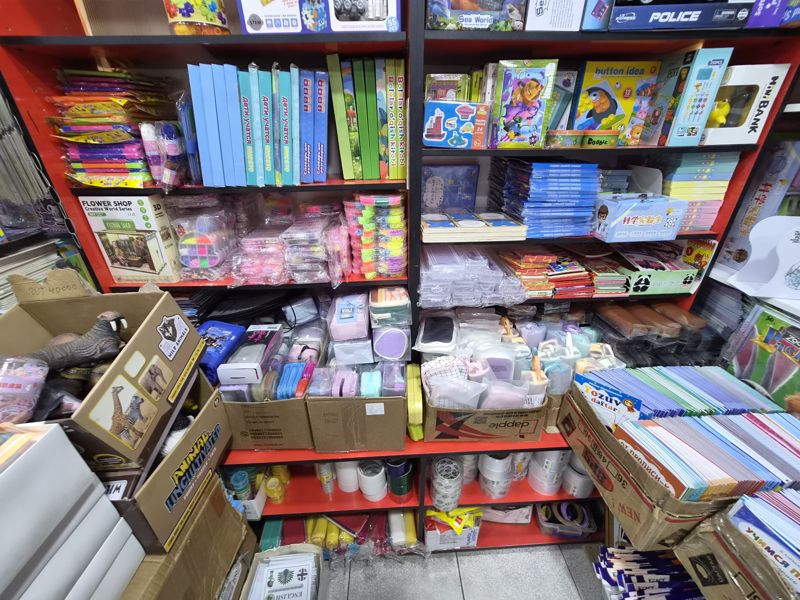 Азбука: красные полки с детскими развивающими играми, наборами для творчества и пеналами, внизу коробки с фигурками животных и скотчем, справа тетради