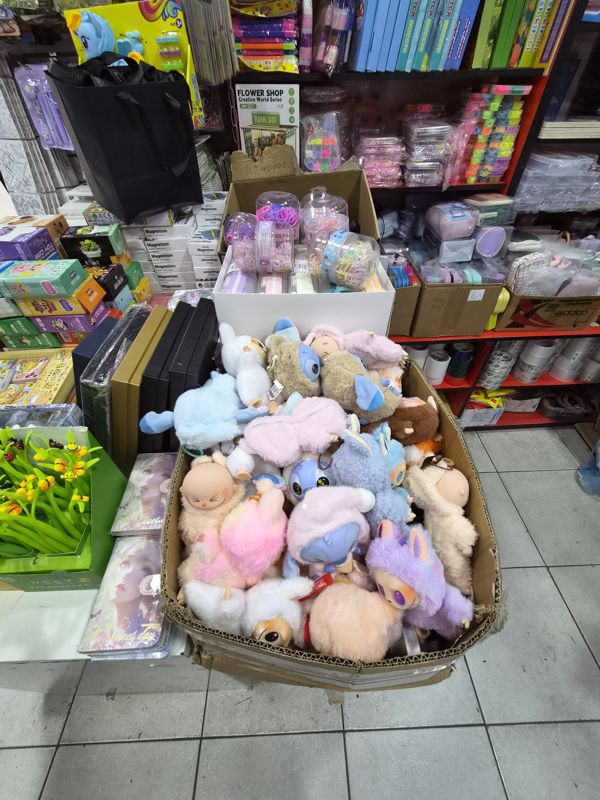 Азбука: большая коробка с плюшевыми игрушками (в том числе в стиле Stitch), рядом блокноты, силиконовые ручки-цветы, нижние полки с клейкой лентой