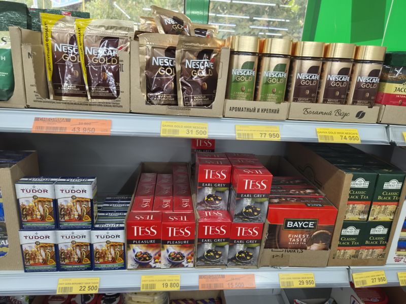 Havas: растворимый кофе Nescafe Gold в пакетах и стеклянных банках на верхней полке, на нижней чай Tudor, Tess, Bayce, Ahmad Tea; жёлтые и оранжевые ценники