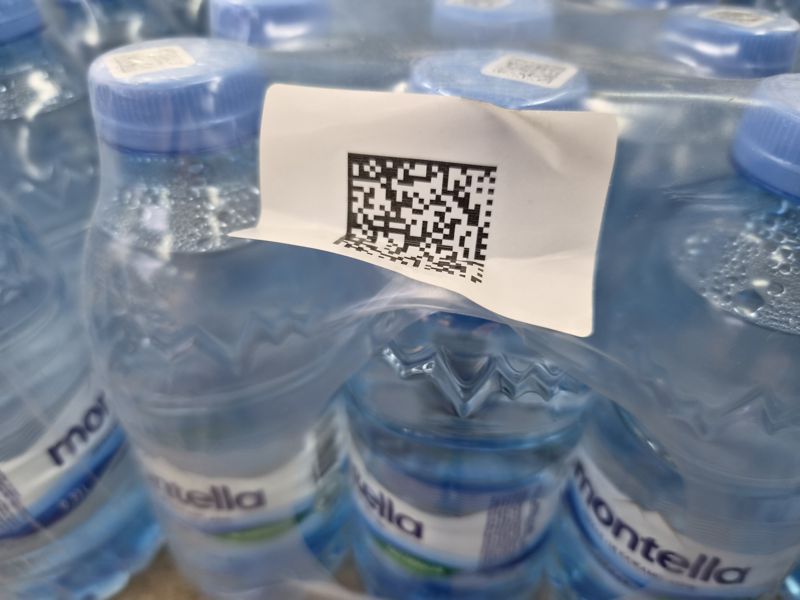 Упаковки воды Montella в плёнке крупным планом: на плёнке белая наклейка с кодом маркировки