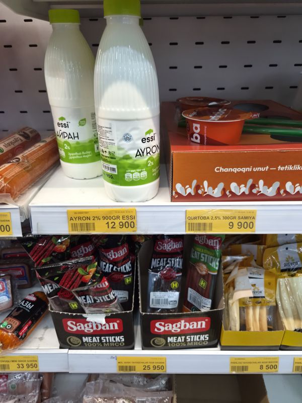 Полка с айраном Essi, Qurtoba Samiya, закуской Sagban Meat Sticks и сырными палочками Bisyor; ценники под полкой