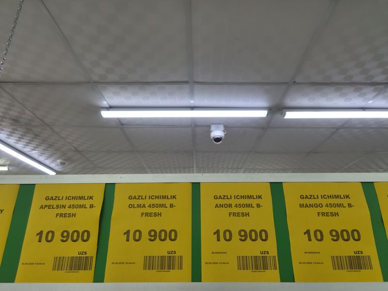Жёлтые ценники B-Fresh на газировку 450 мл под потолком: апельсин, яблоко, гранат, манго; вверху купольная камера видеонаблюдения