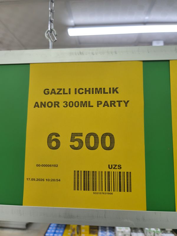 Крупно жёлтый ценник под потолком: газированный напиток Party гранат 300 мл, 6 500 сум; на заднем плане светильник и полки