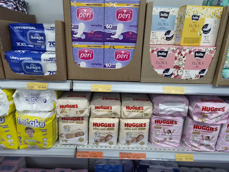 Havas: полка с влажными полотенцами Sunlight XXL, ежедневными прокладками Peri и Bella Flora; ниже подгузники Huggies Elite Soft (два оранжевых ценника CHEGIRMA), трусики LaLaku и Huggies Ultra Comfort для девочек