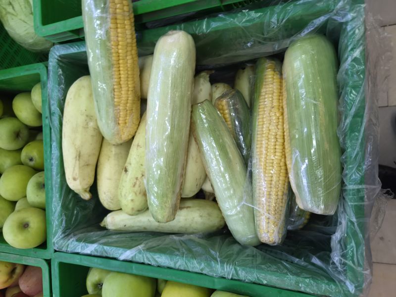 Ящик с початками сладкой кукурузы и белыми кабачками, часть упакована в стрейч-плёнку; слева зелёные яблоки